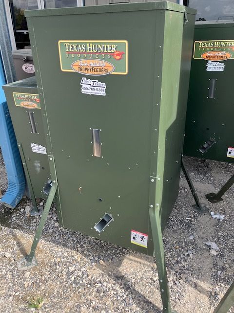 A green texas hunter feeder is sitting on top of a gravel road.