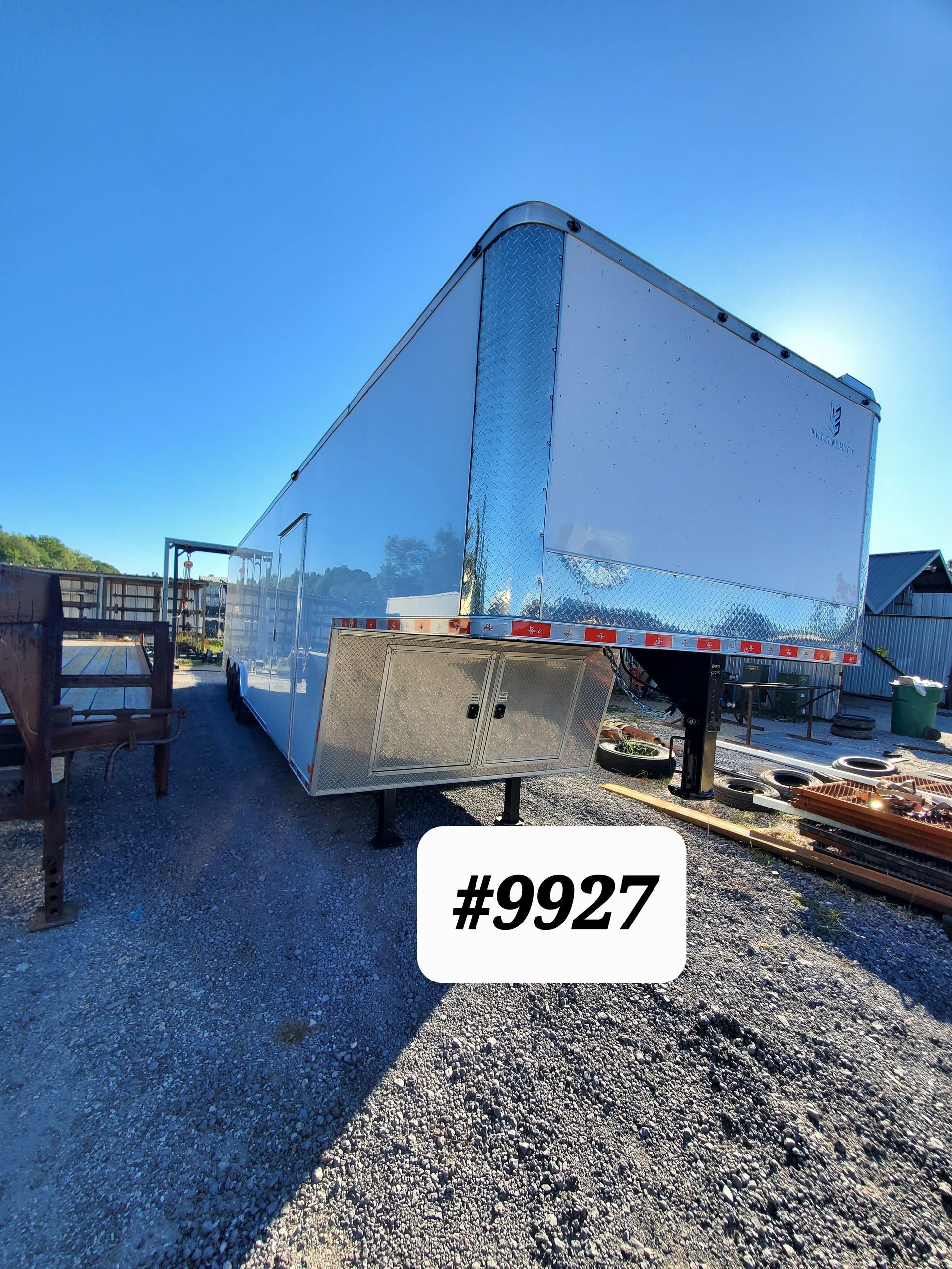 A white trailer with the number 9927 on it is parked in a gravel lot.