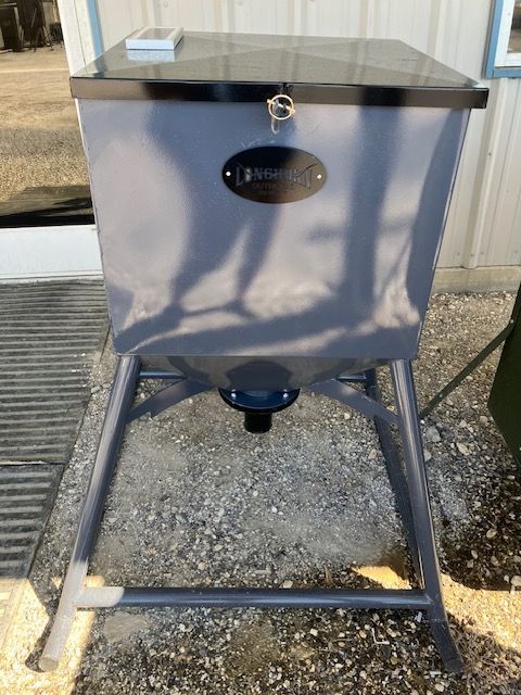 A gray metal container with a lock on the lid is sitting on the ground.