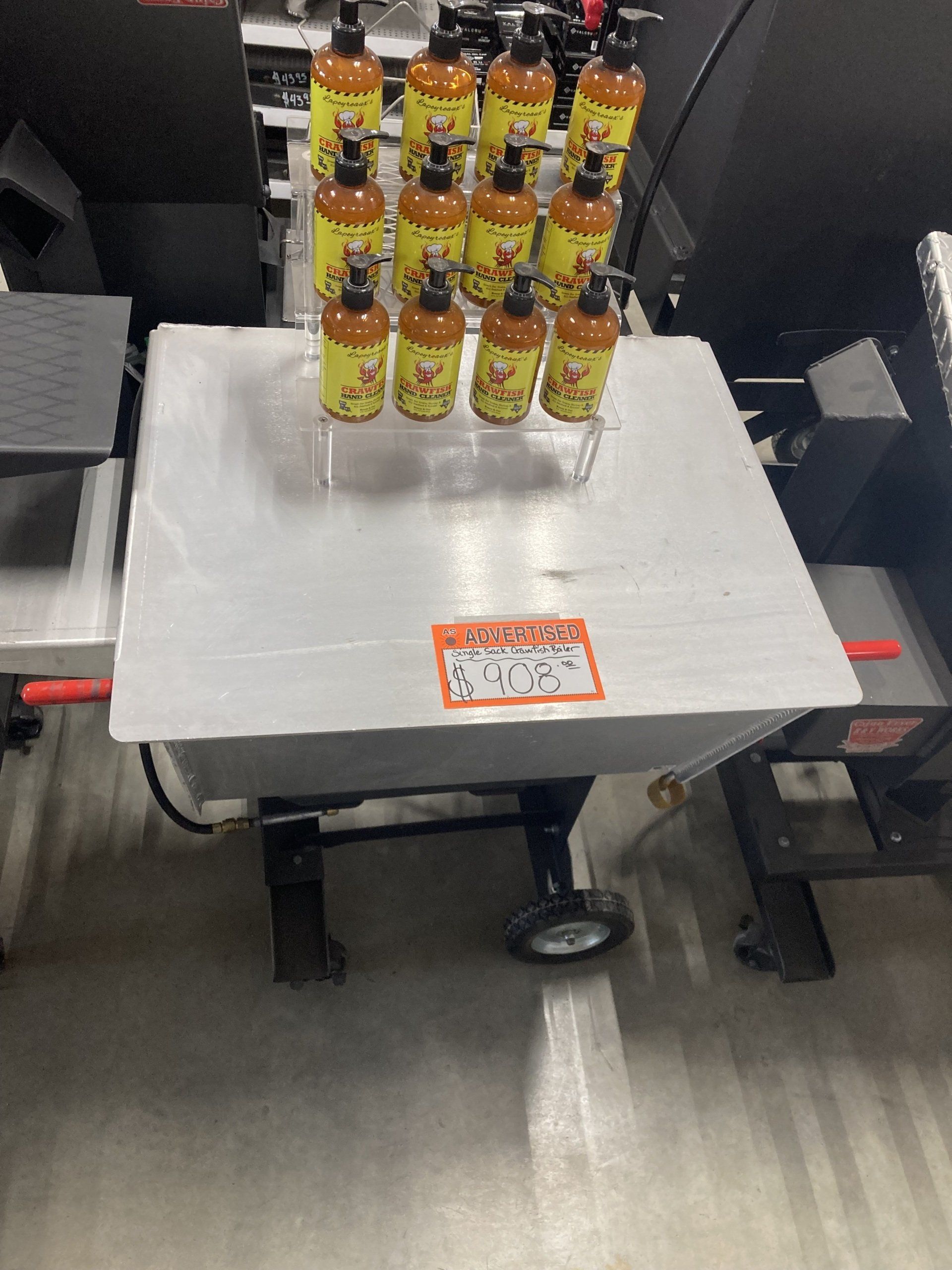 A wheelbarrow filled with bottles of hot sauce on a table.