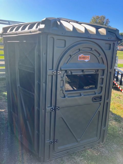 A small shed with a door and a window is sitting in the grass.