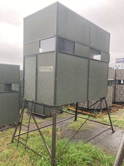 A deer blind with a ladder attached to it is sitting in a field.