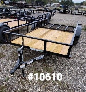 Black utility trailer with wooden deck on gravel, with the number 10610 displayed.