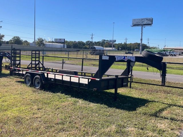 Black gooseneck trailer on grass, with two axles, in a sunny outdoor setting.
