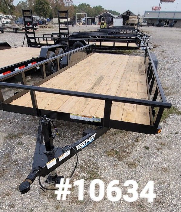 Black trailer with wooden deck, safety rails, and trailer hitch, parked outdoors.