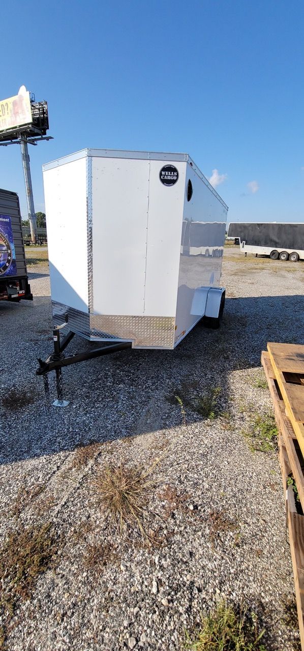 White enclosed cargo trailer on gravel under a blue sky.