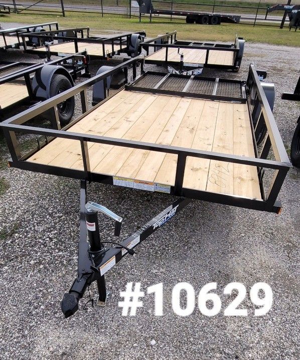 Black utility trailer with wooden deck, black frame and trailer hitch. Gravel lot. #10629 is in white.