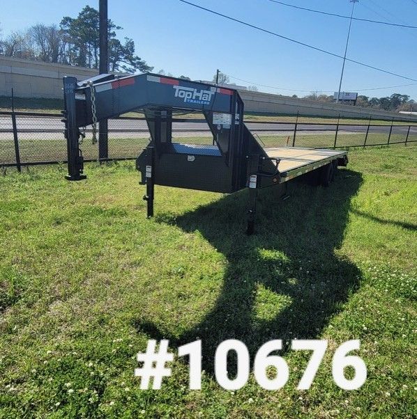 A black Top Hat gooseneck flatbed trailer on green grass. The trailer has a wooden deck.