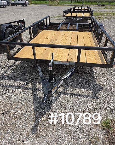 Black utility trailer with wooden floor, front jack, and mesh ramps on gravel lot.