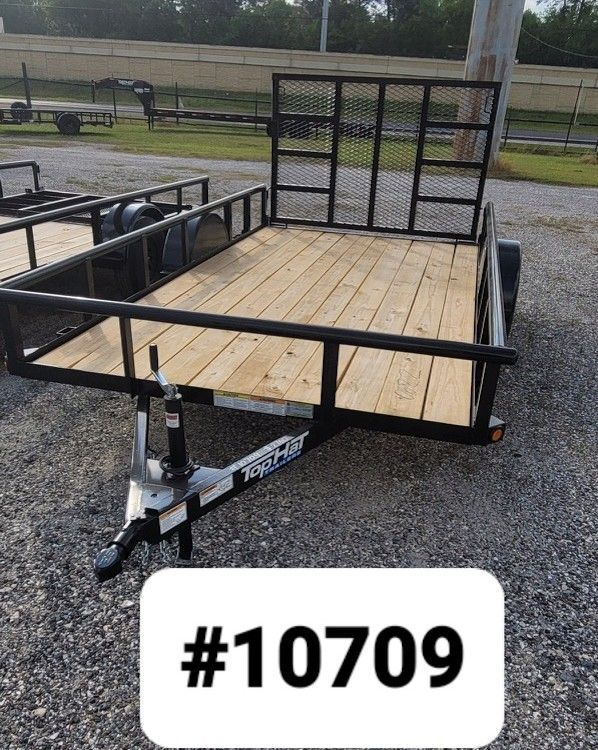 A black metal utility trailer with a wooden floor and a rear mesh gate parked on a gravel lot, labeled with #10709.