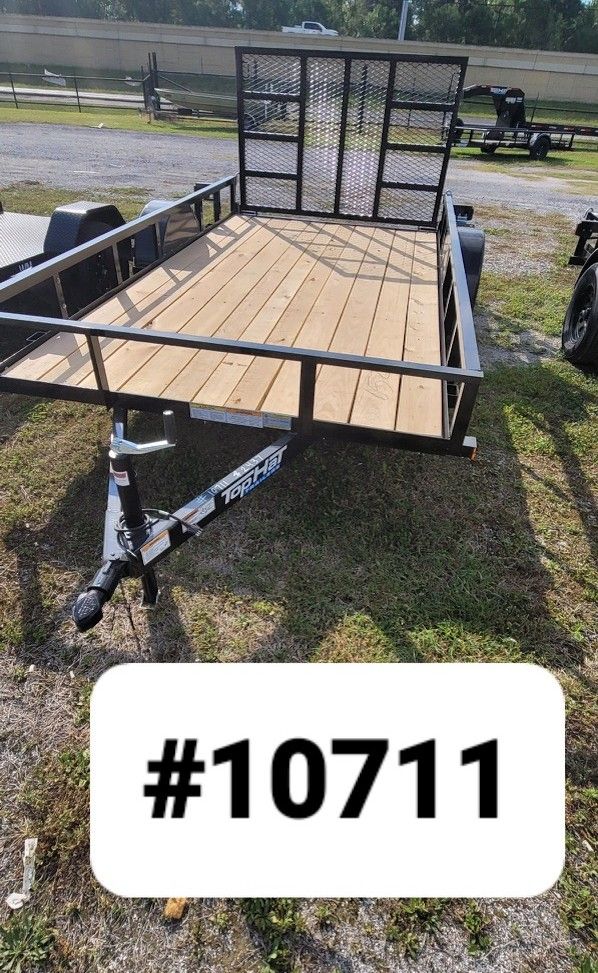 A new black utility trailer with a wooden floor and a rear mesh gate parked on a gravel lot, labeled with text #10711.
