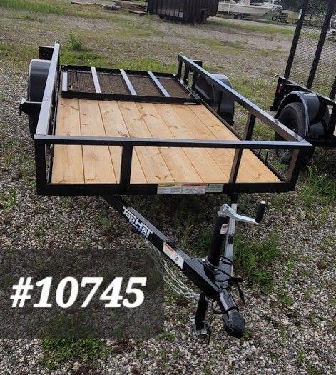 Small black utility trailer with wooden floor and mesh sides on gravel, labeled #10745