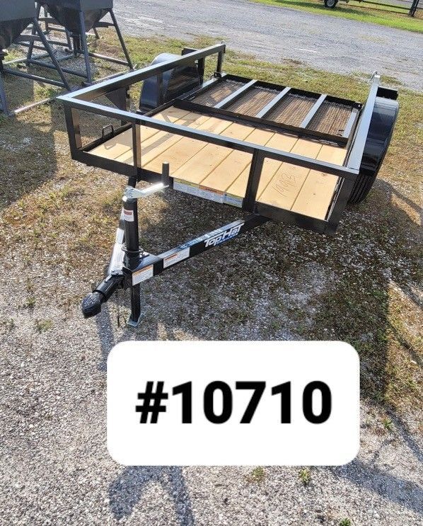 A small, new black utility trailer with wooden flooring, parked on a gravel lot, labeled #10710.