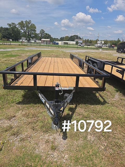Utility trailer with wooden deck and black metal rails parked on a grassy lot