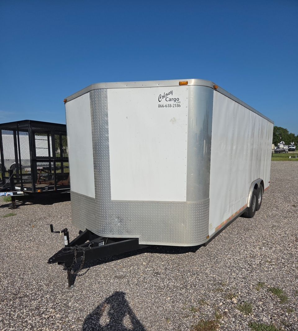 White enclosed cargo trailer parked on gravel under a clear blue sky.