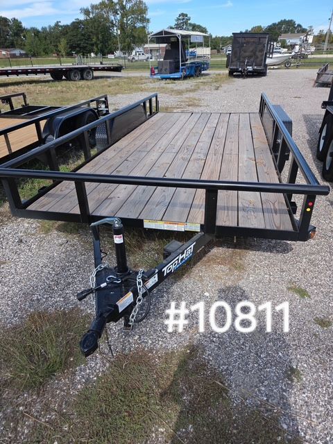 Black utility trailer with wooden deck and rails parked on gravel lot, front view