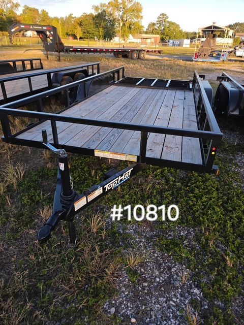 Black flatbed trailer with wooden deck parked on grass by a canal at sunset