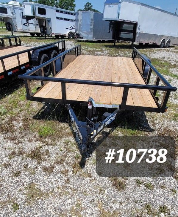 Black flatbed utility trailer with wooden deck and railings in a gravel lot, marked #10738