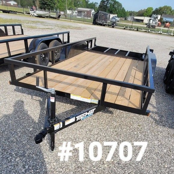 A black utility trailer with a wooden deck parked on a gravel lot, labeled with the number #10706.