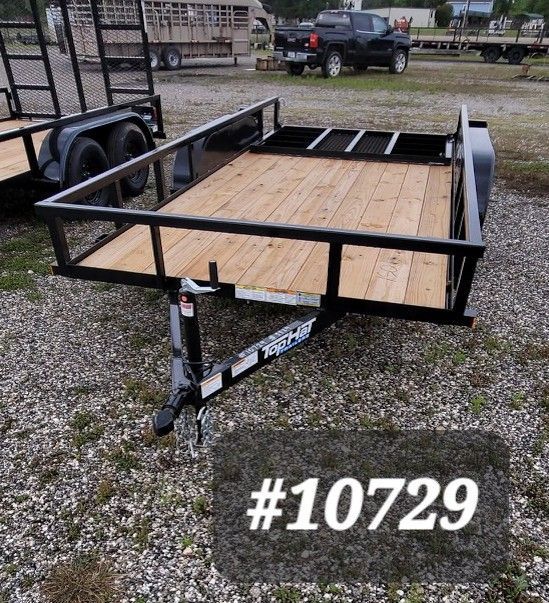 Black utility trailer with wooden floor and black metal frame parked on gravel, marked #10729
