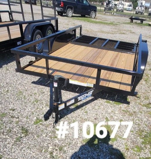 Black trailer with wooden deck, black railings, parked on gravel.