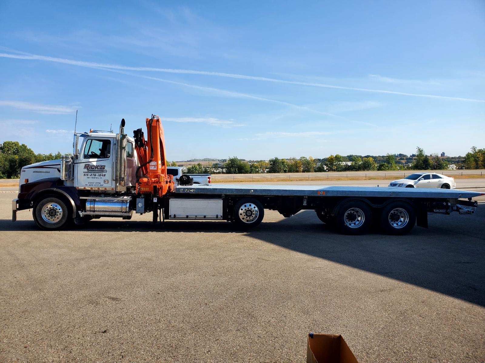 A flatbed tow truck with a crane attached to it is parked on the side of the road.