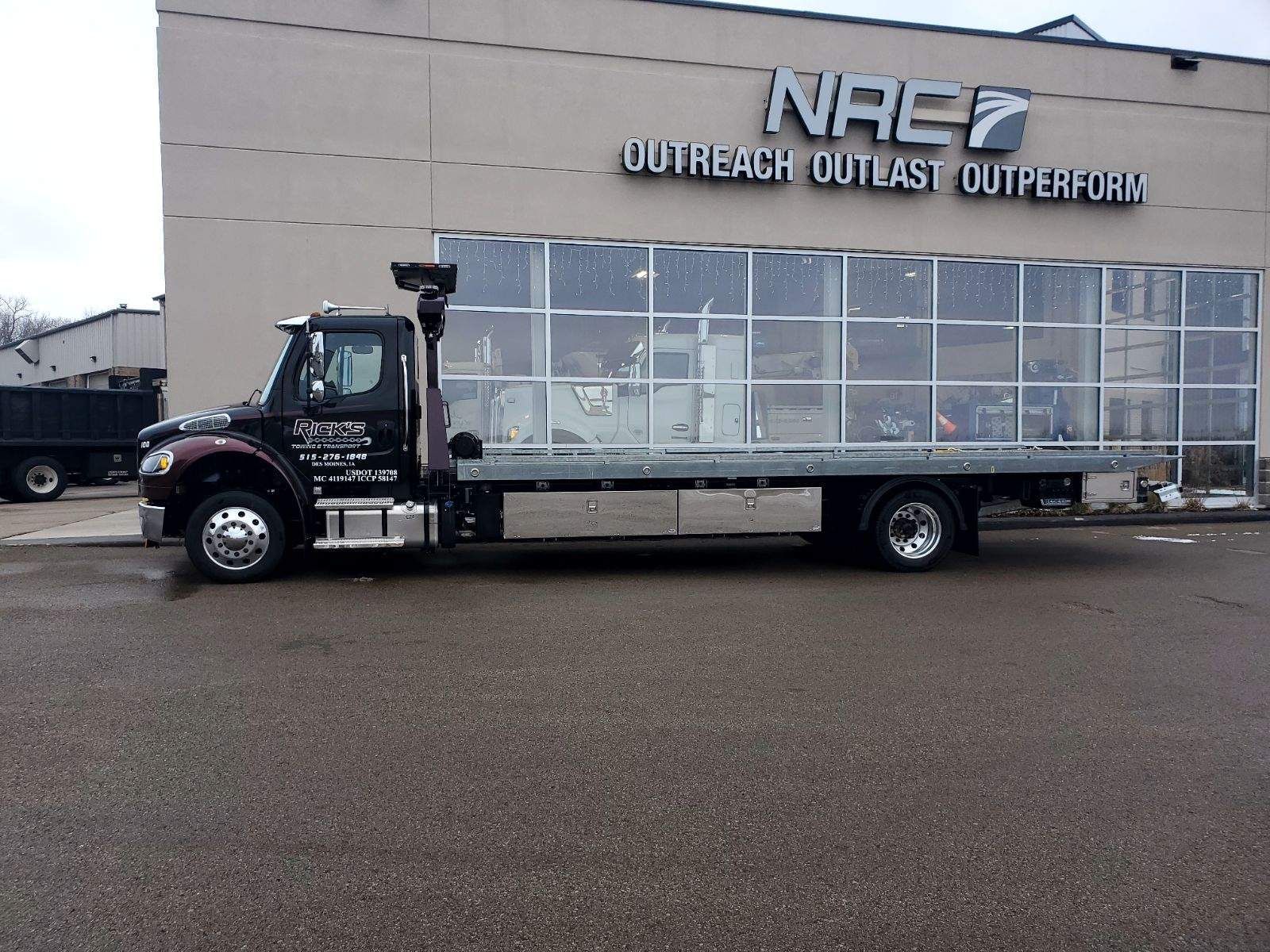 A flatbed tow truck is parked in front of a building.