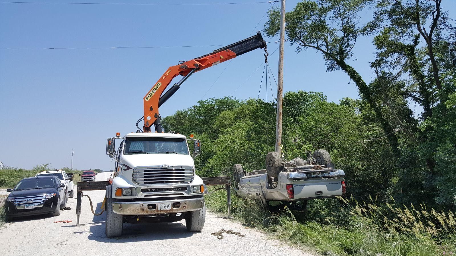 A truck with a crane attached to it is towing a truck that has fallen off the road.