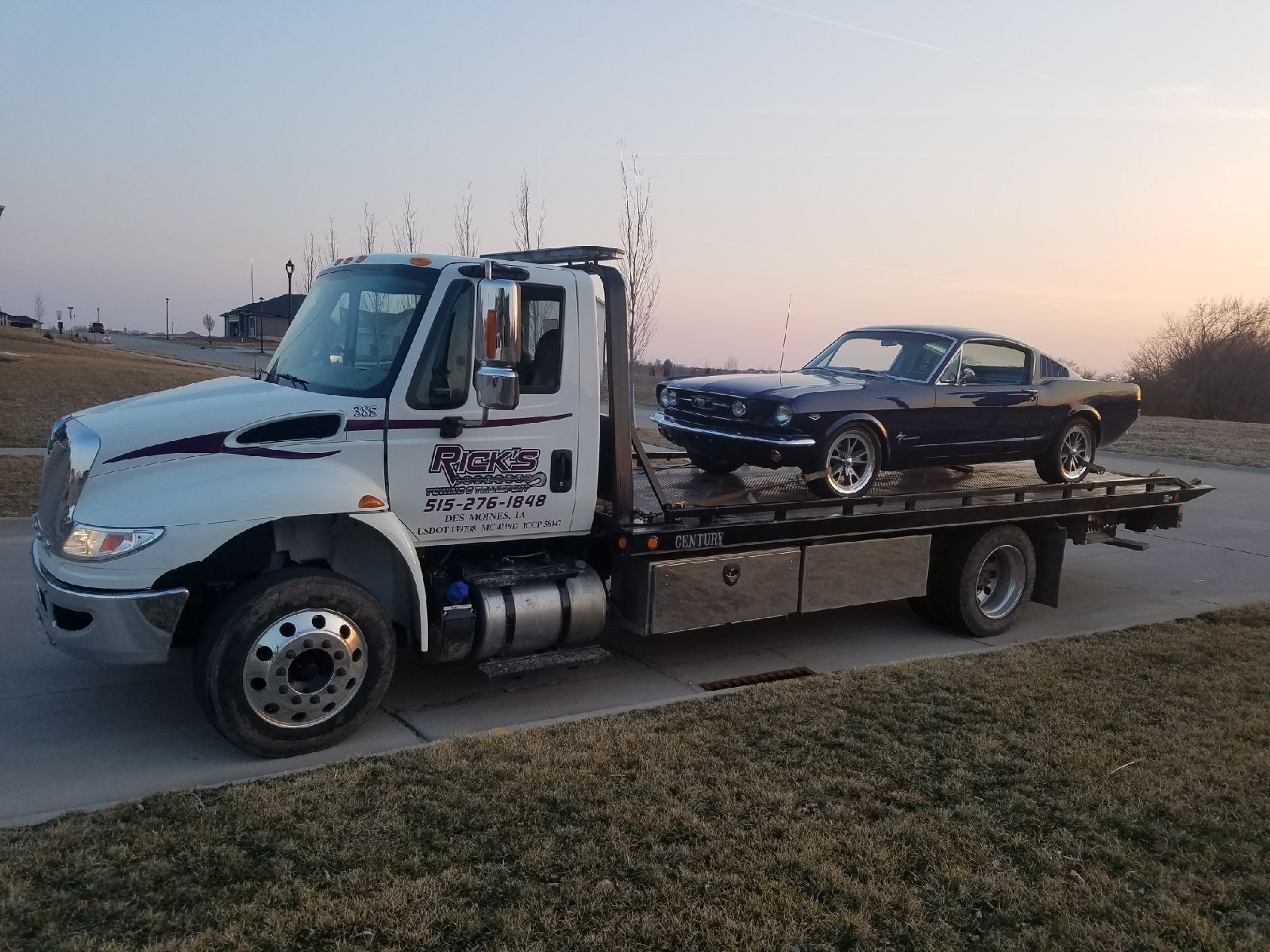 A tow truck is carrying a mustang on the back of it.