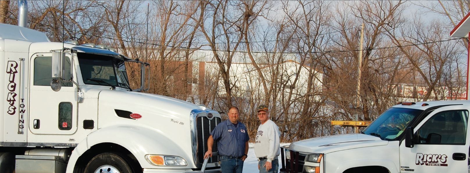 Two men are standing next to a semi truck and a tow truck.