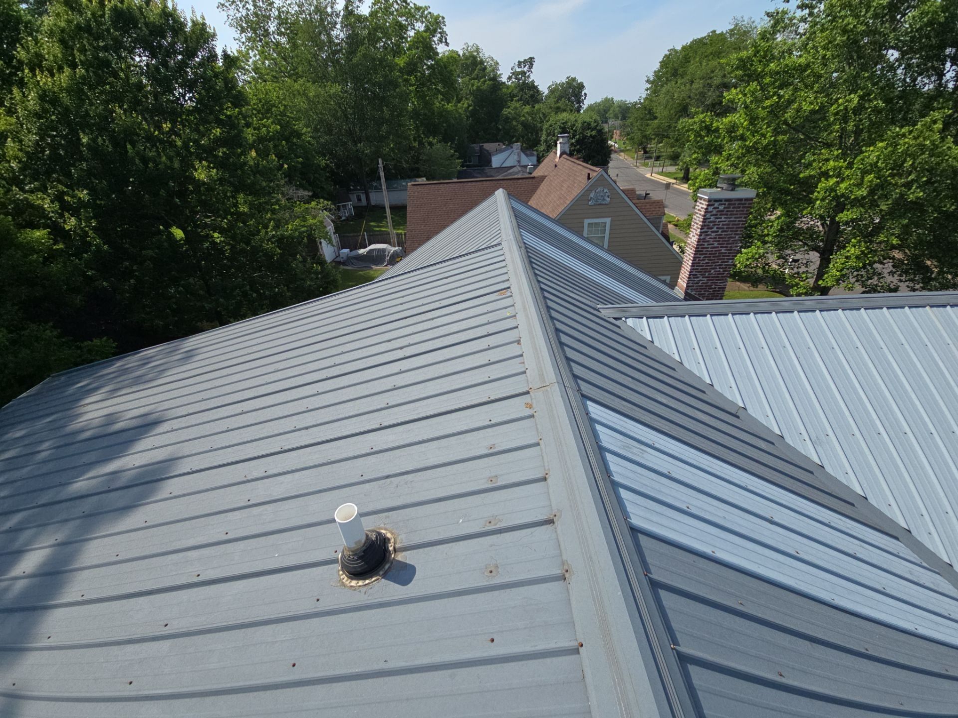 Metal roof, angled view; houses and trees visible in the background on a sunny day.