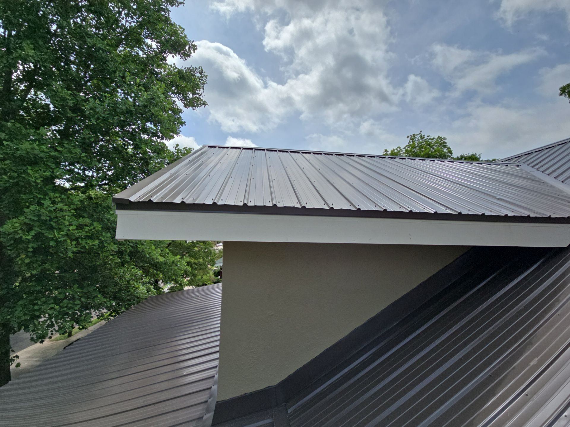 Brown metal roof of a building with white trim under a cloudy sky.