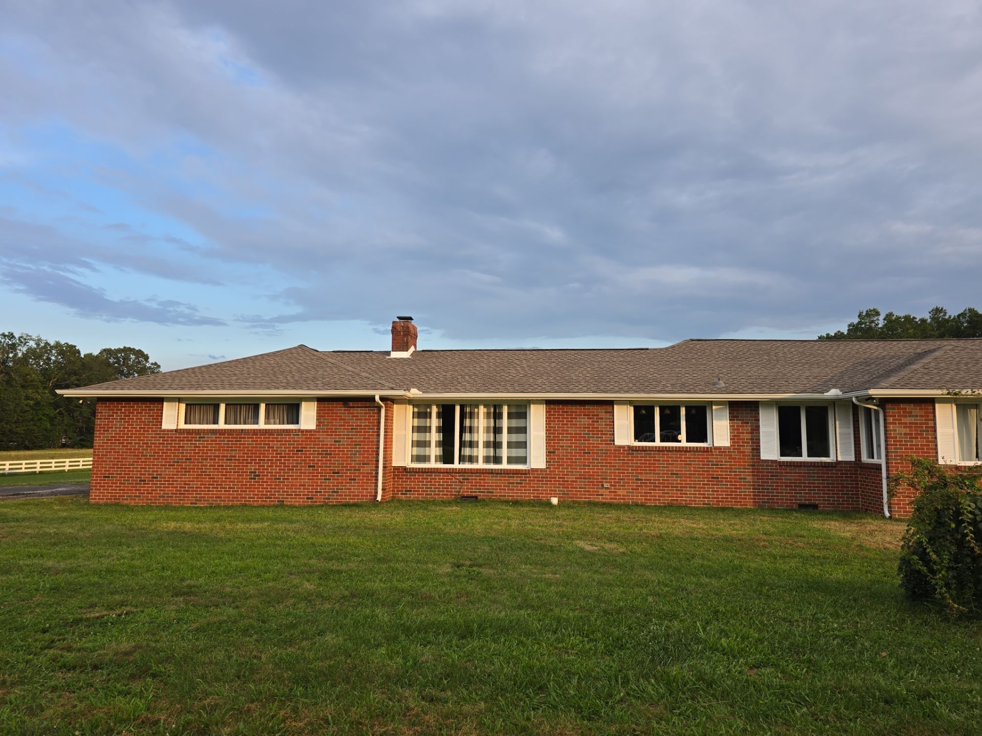 Red brick ranch house with white trim, green lawn, cloudy sky.