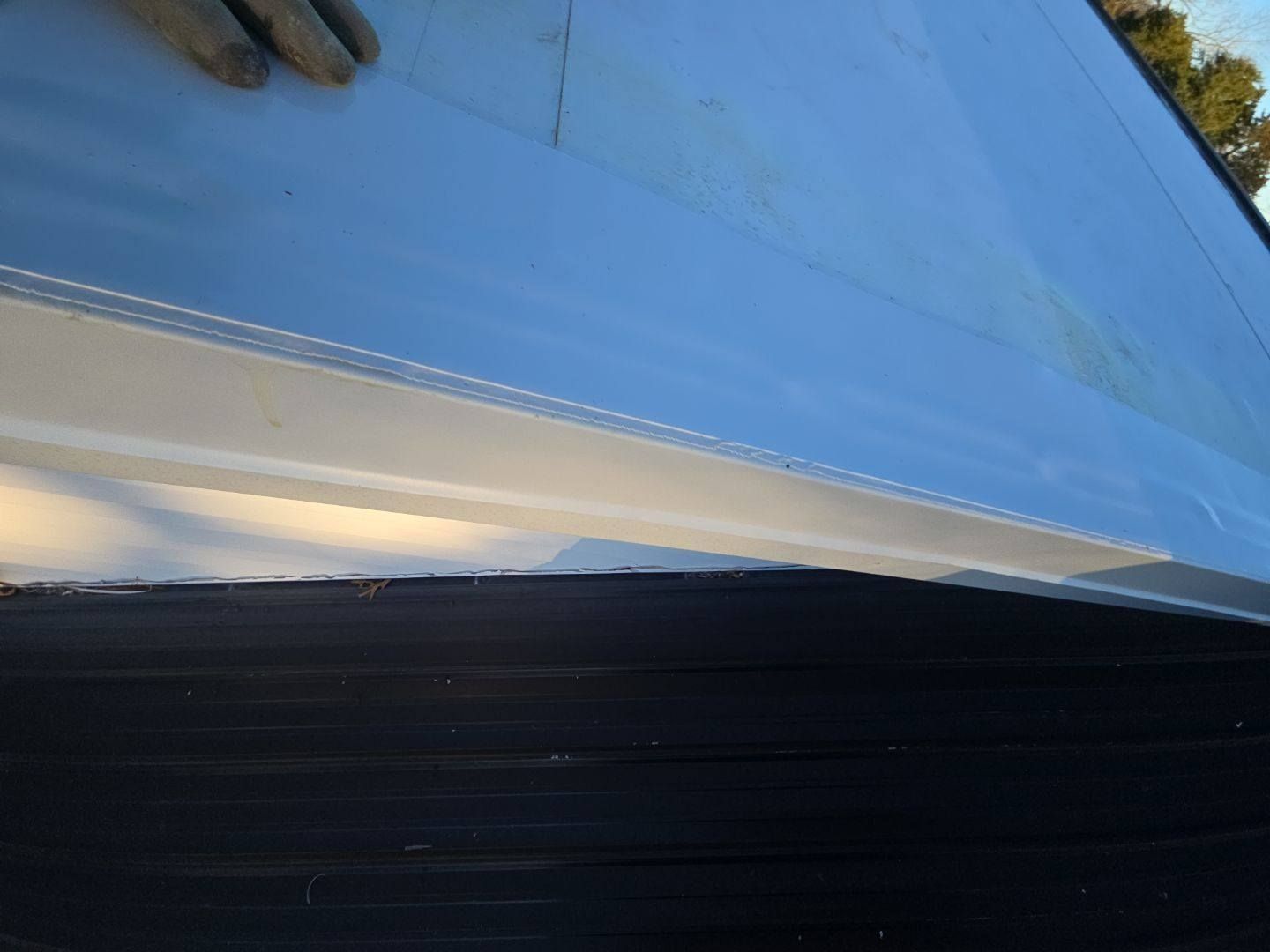 Close-up of white gutter being installed on a dark roof. A gloved hand holds the gutter.