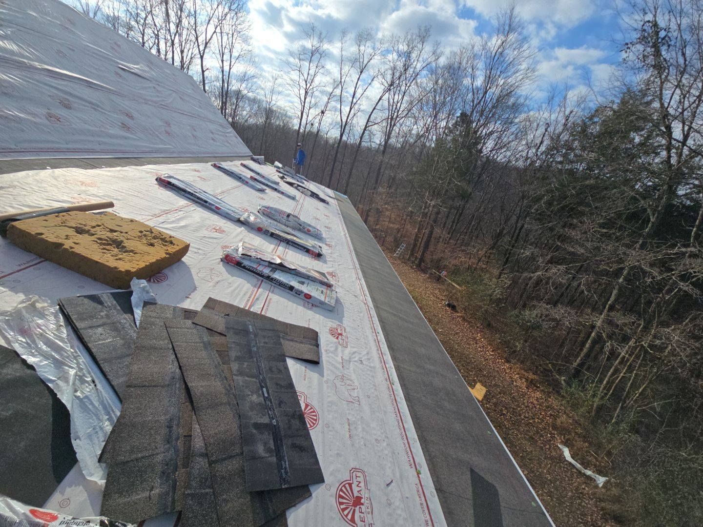 Roofing work in progress, asphalt shingles and protective underlayment on roof.