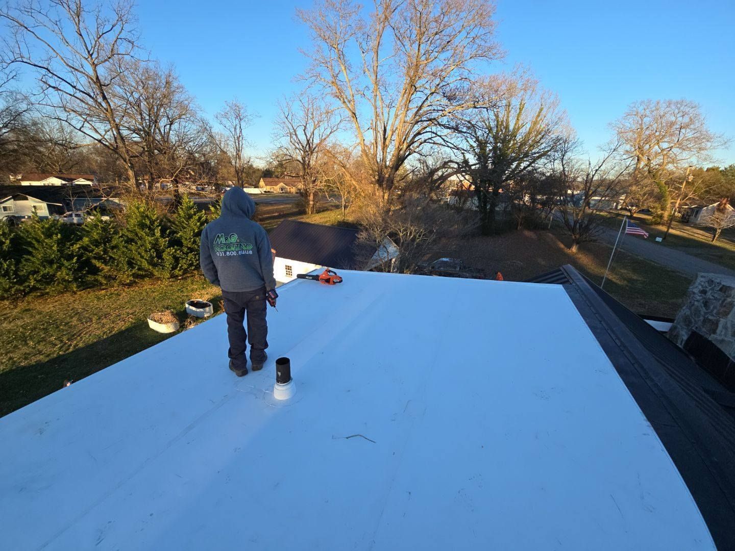 Person on a white flat roof with trees in the background, a sunny day.