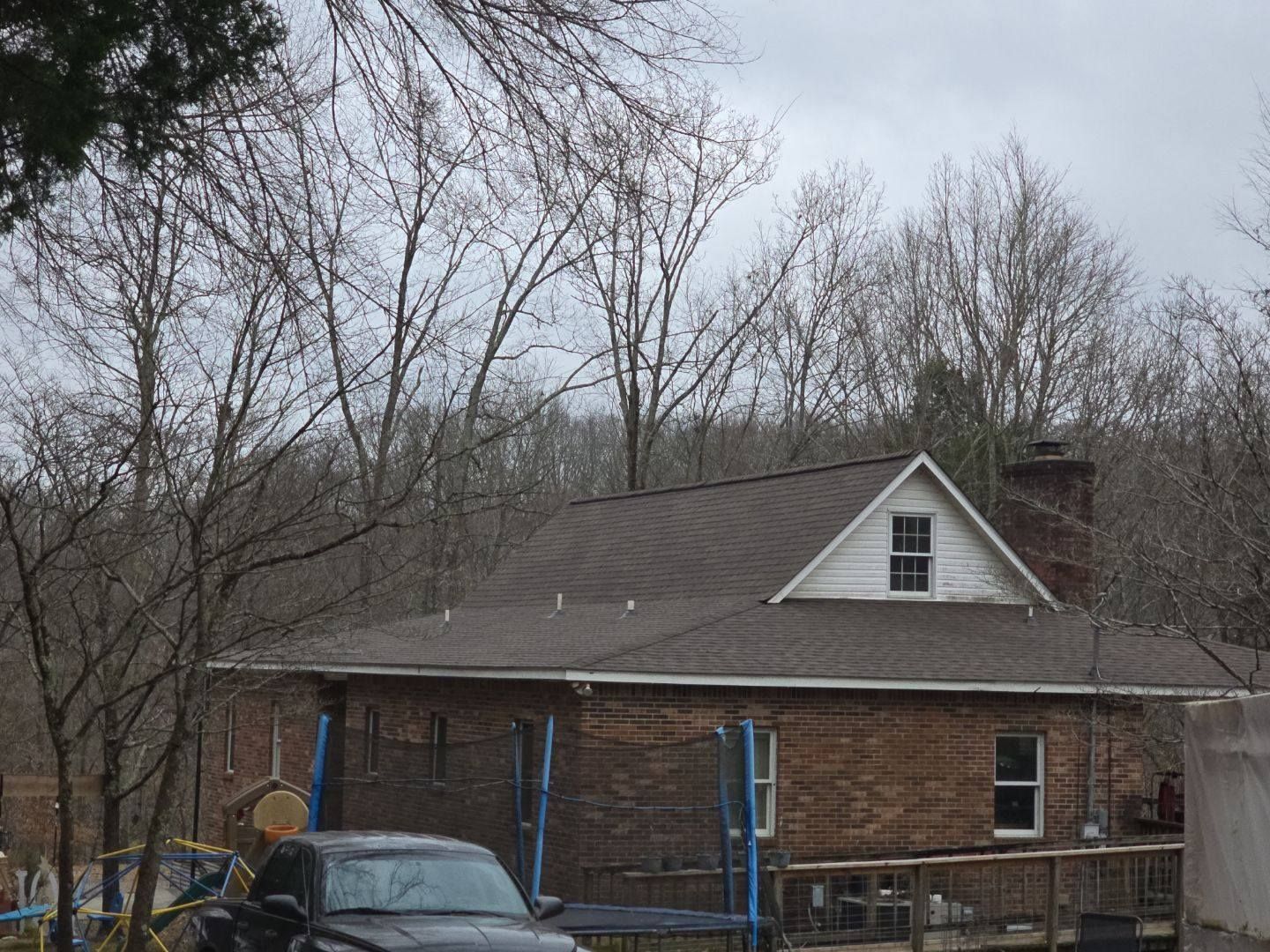 House with brick exterior, brown roof, and small white gable. Bare trees in background.