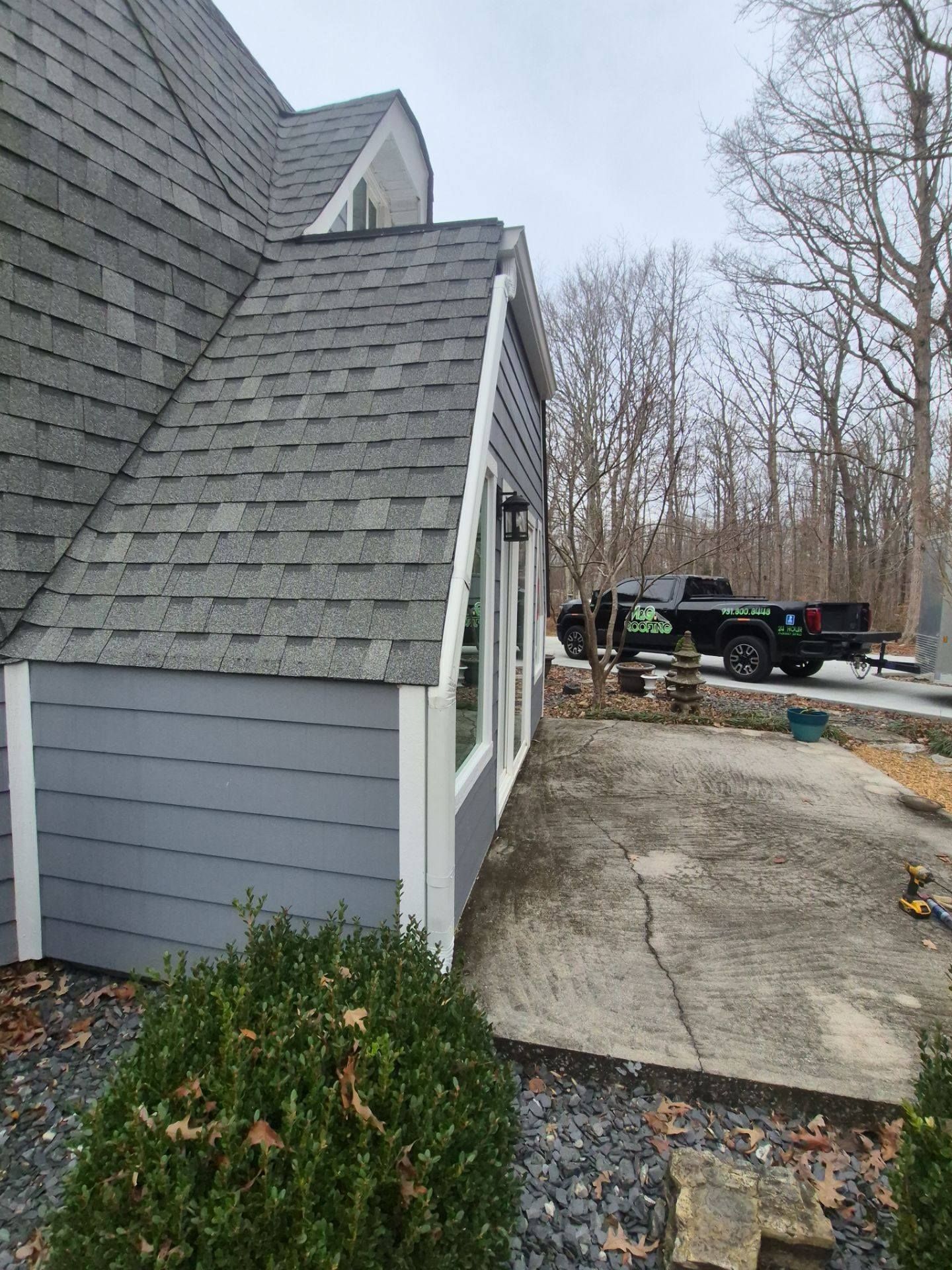 Gray house with shingled roof, blue siding, white trim, concrete walkway, and a truck in the background.