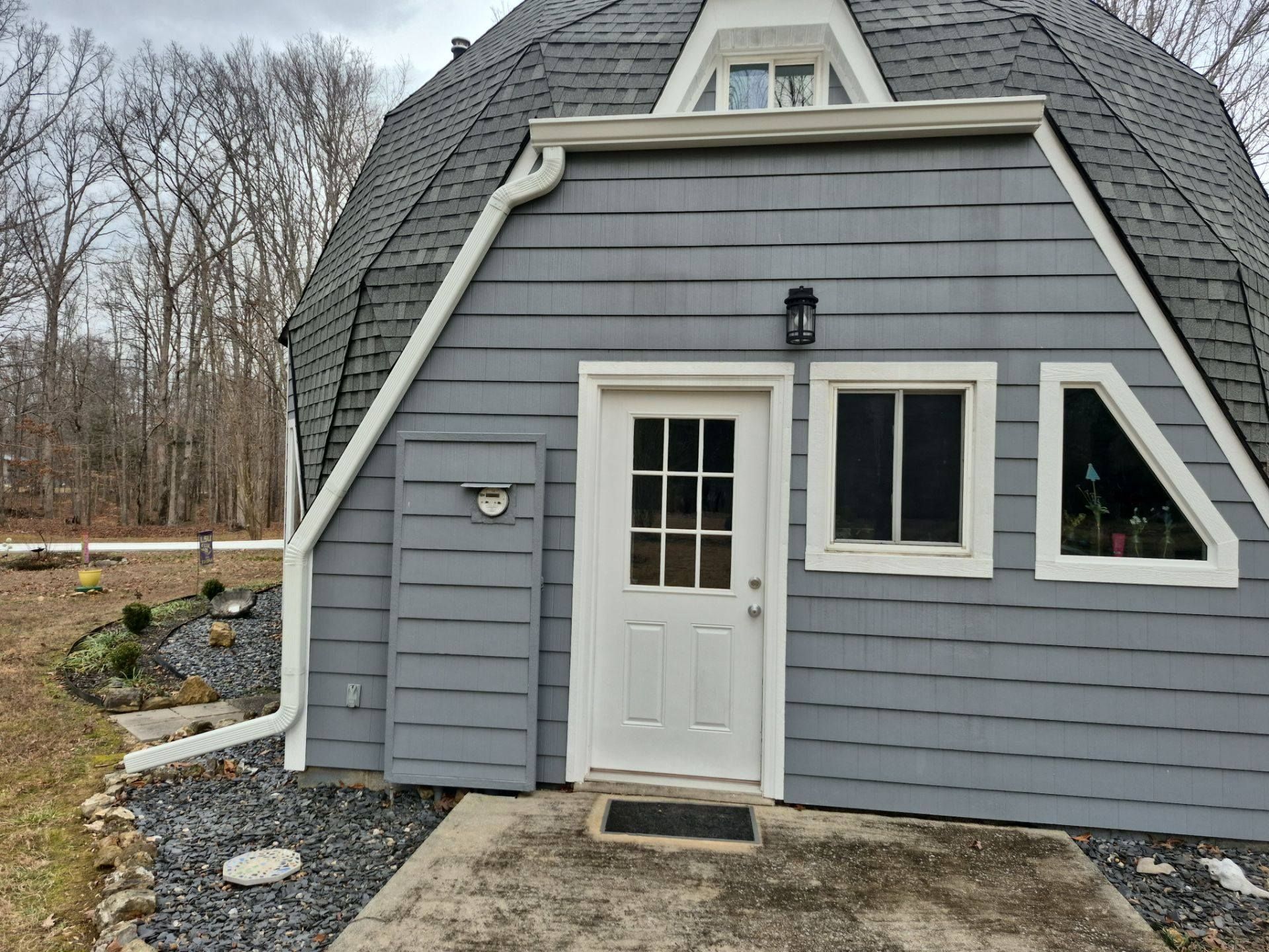 Gray dome-shaped house with white trim, door, and windows. Black roof and a small porch.