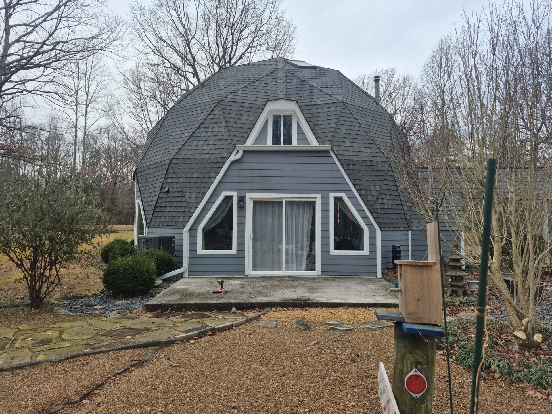 Geodesic dome house with gray exterior and triangular windows and a small chimney.