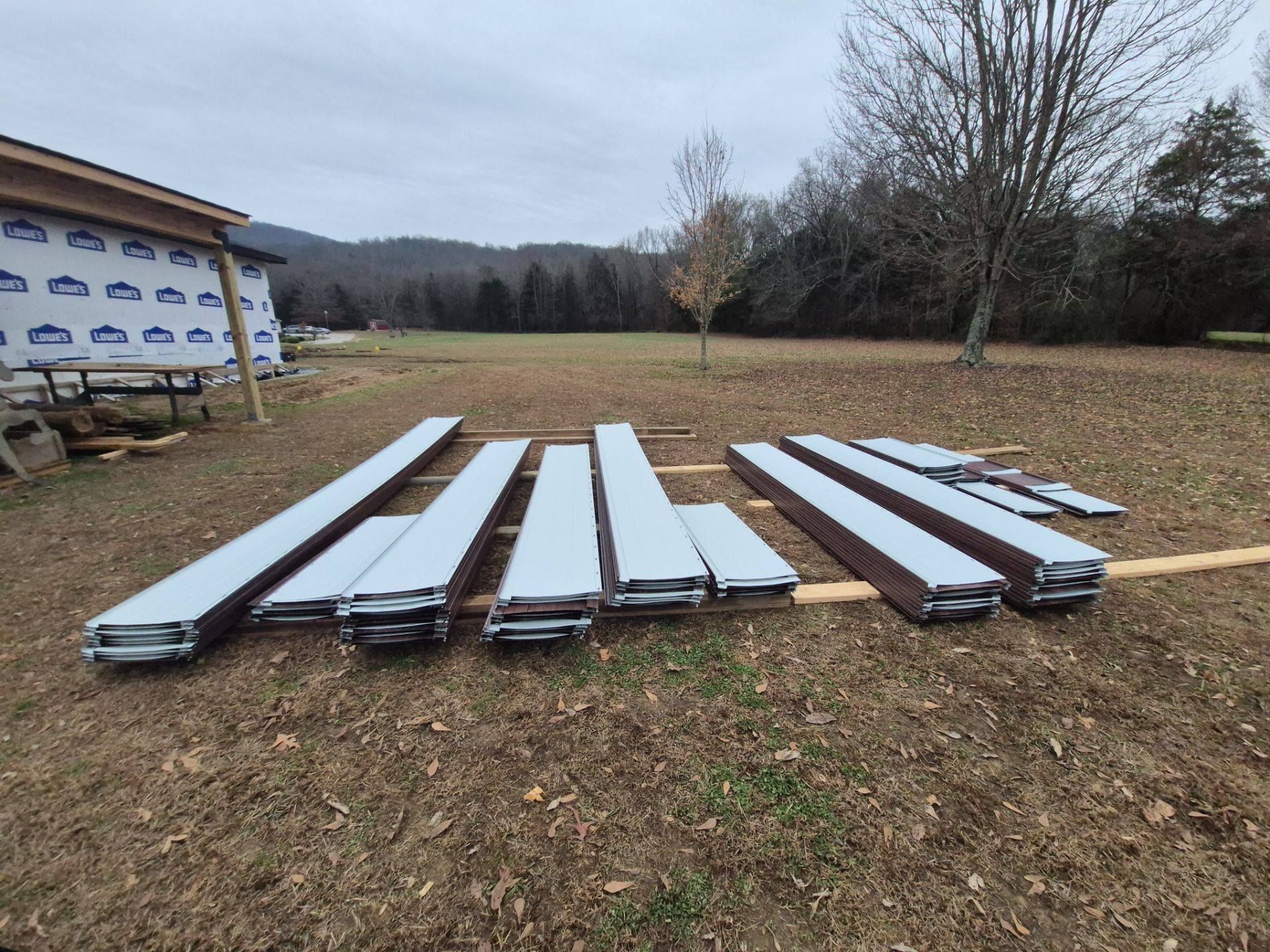 Metal building components laid out on brown grass in front of a construction site.