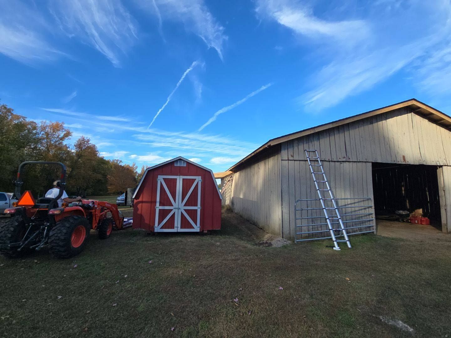 Tractor pulling a red shed next to a weathered barn on a sunny day with blue sky.