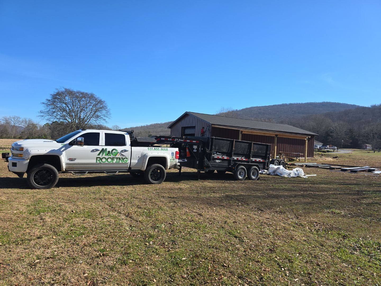 White pickup truck towing a trailer with landscaping supplies near a building in a field.