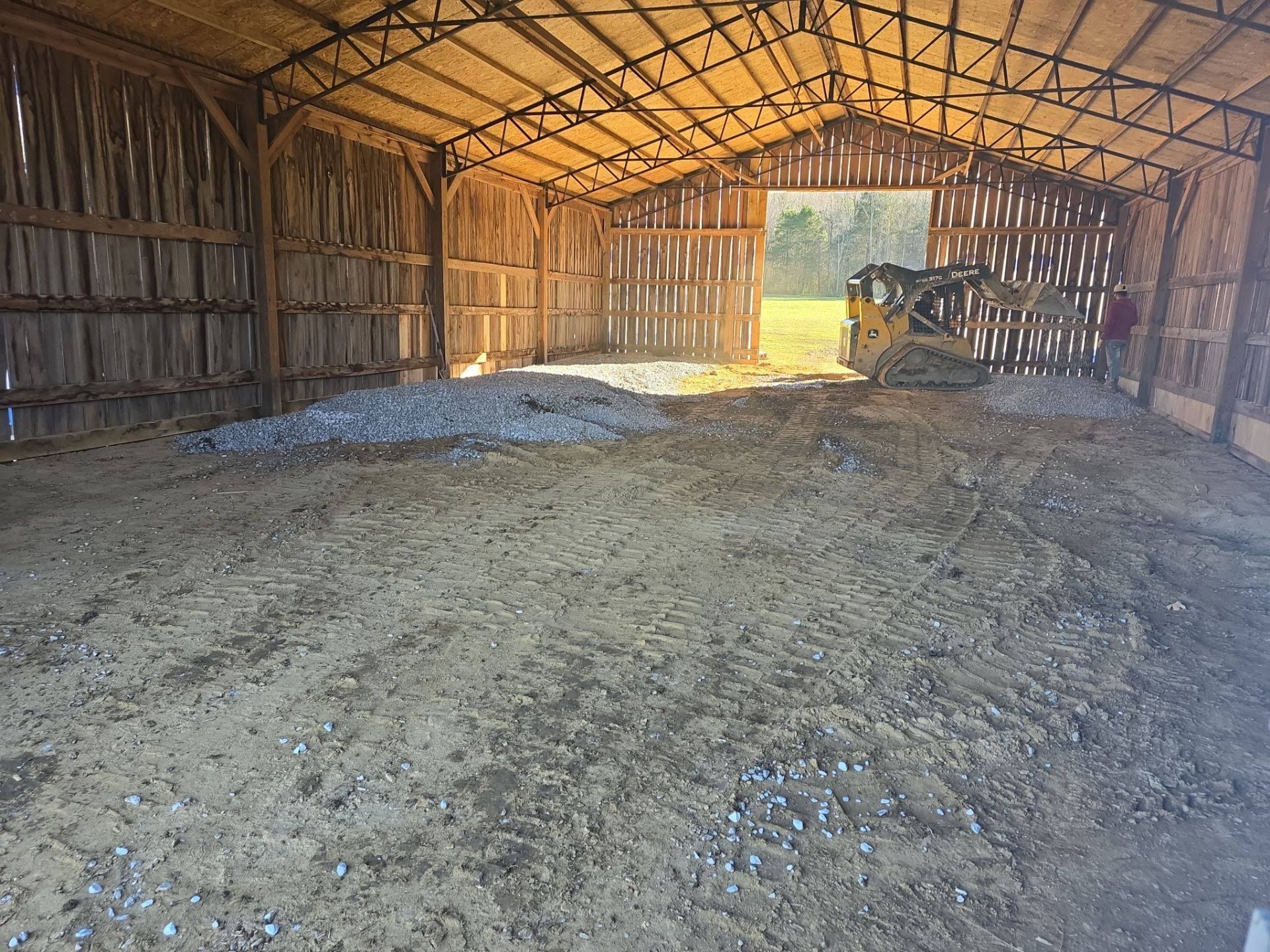 Interior of a barn with a gravel floor and a small construction vehicle.