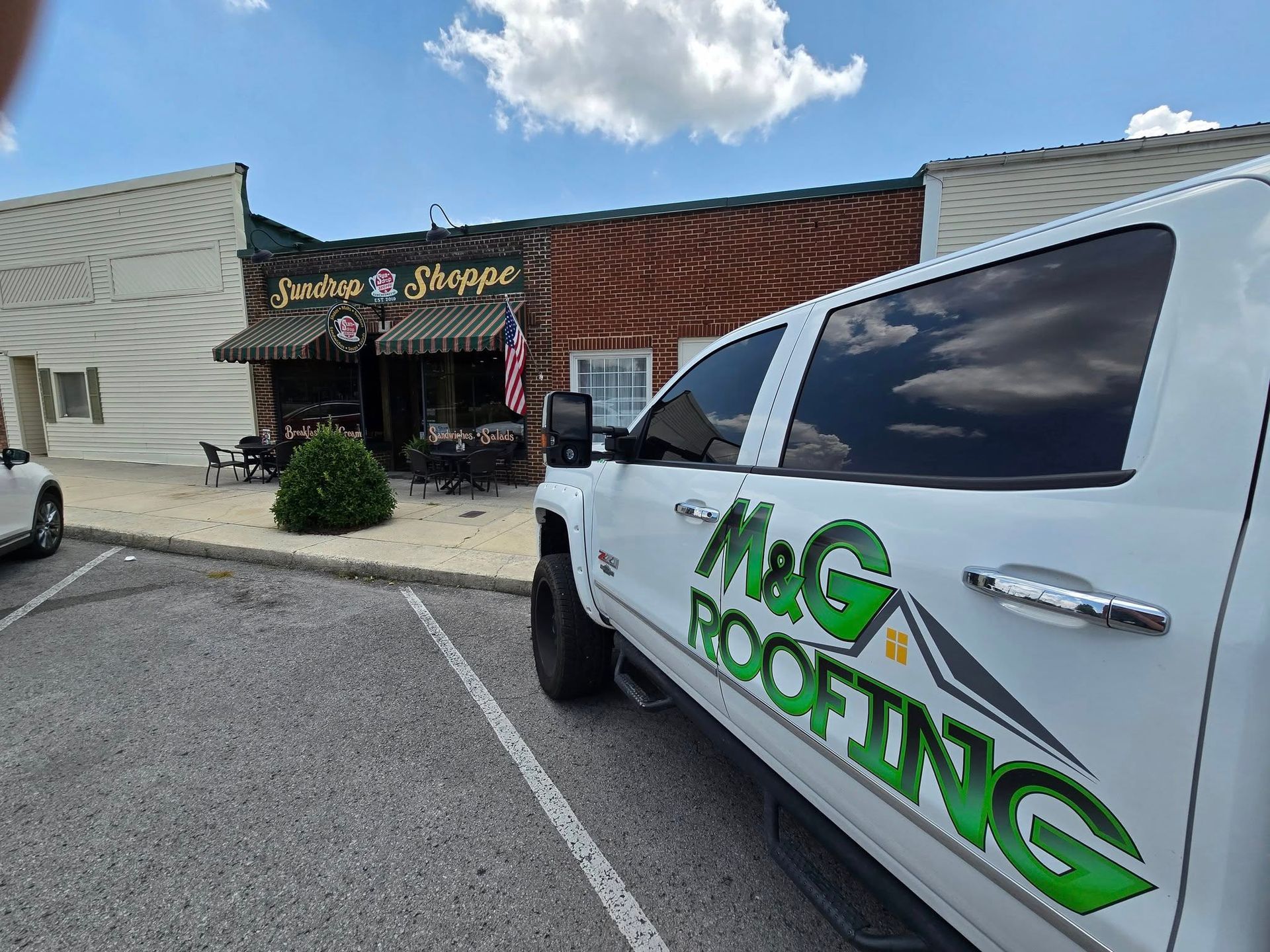 White M&G Roofing truck parked in front of a brick building labeled 