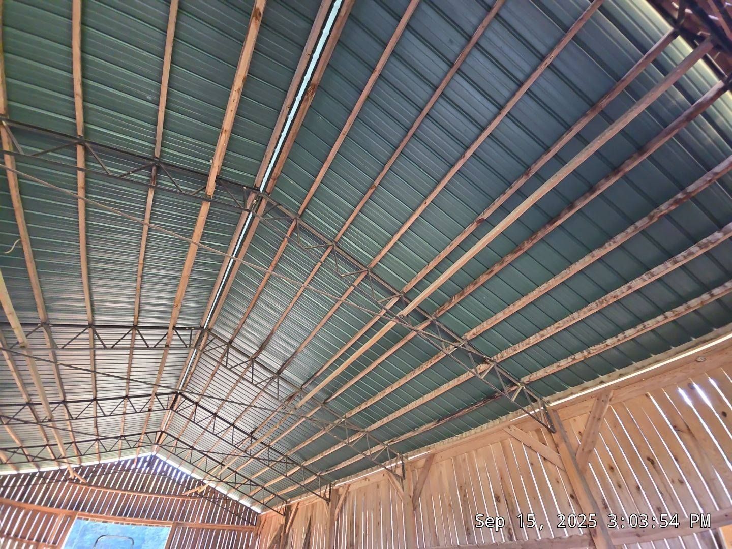 Interior view of a barn roof with green metal panels, wooden beams, and natural light.