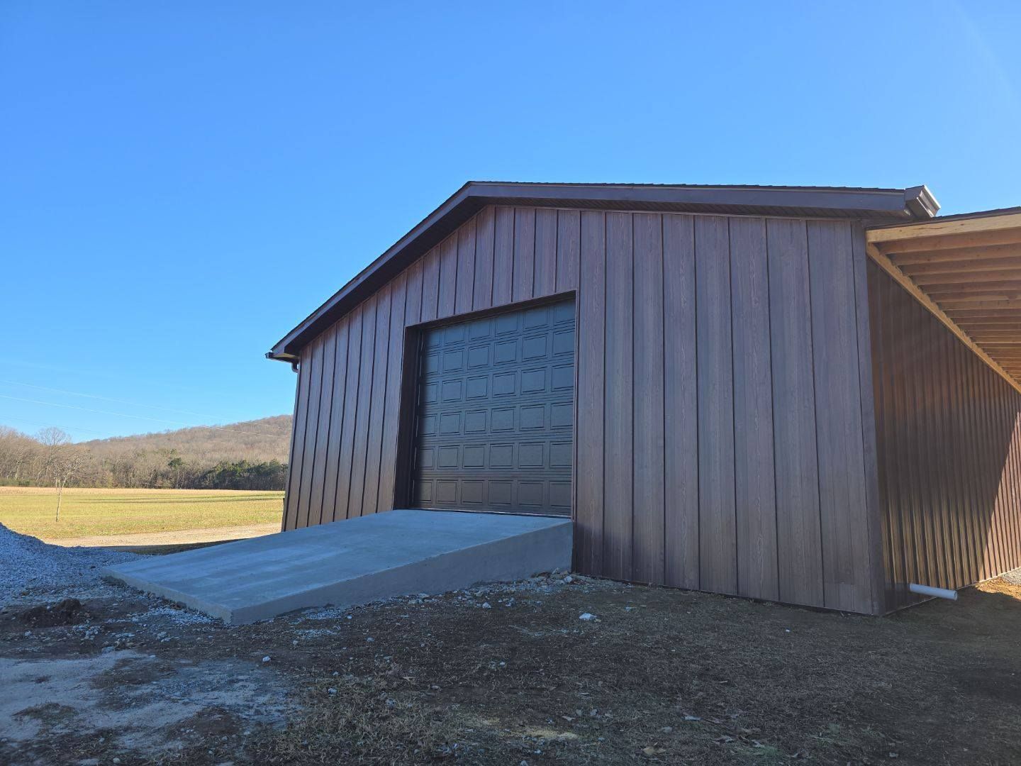 Brown barn with a large black door, concrete ramp, and blue sky.