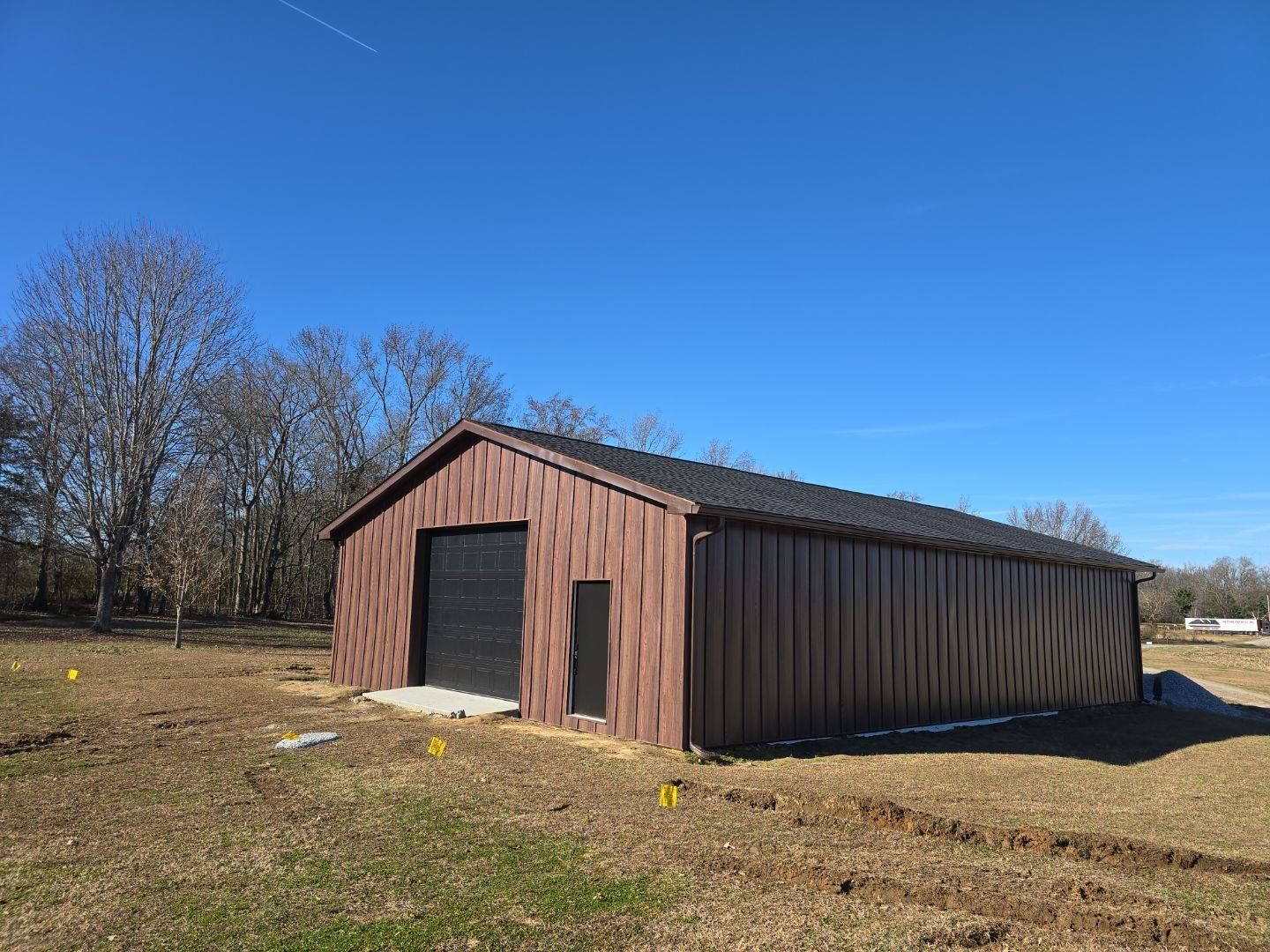Brown metal barn with a black door on a sunny day.