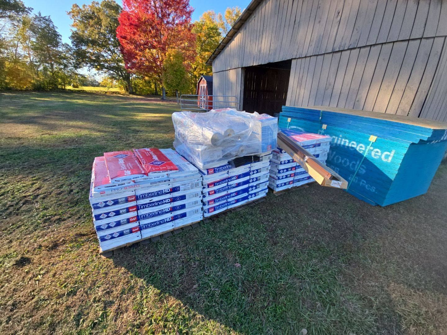 Stacks of blue and red insulation materials, and wood on grass, next to a barn.