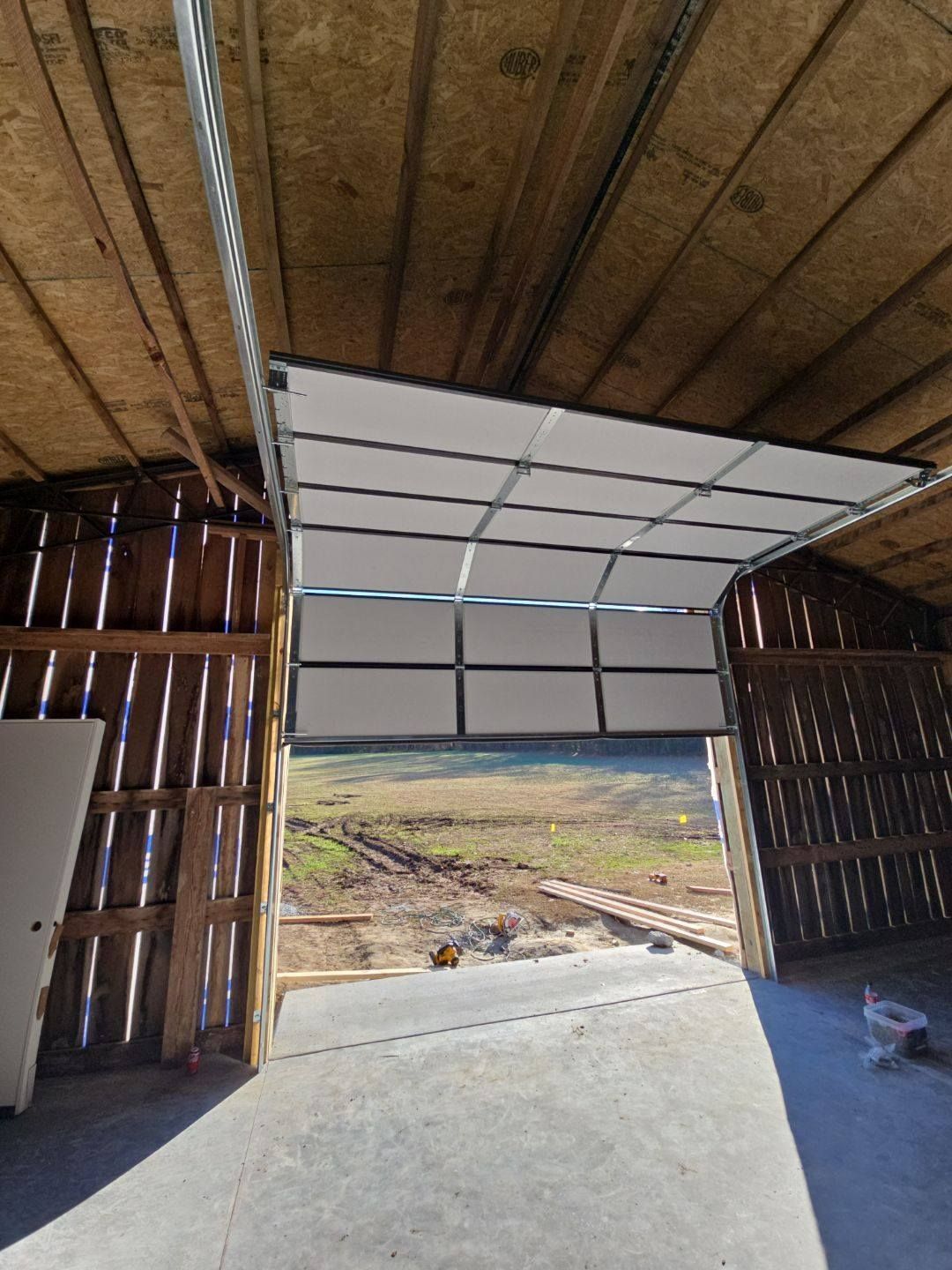 A partially open white garage door on a wooden barn, with an outdoor view.